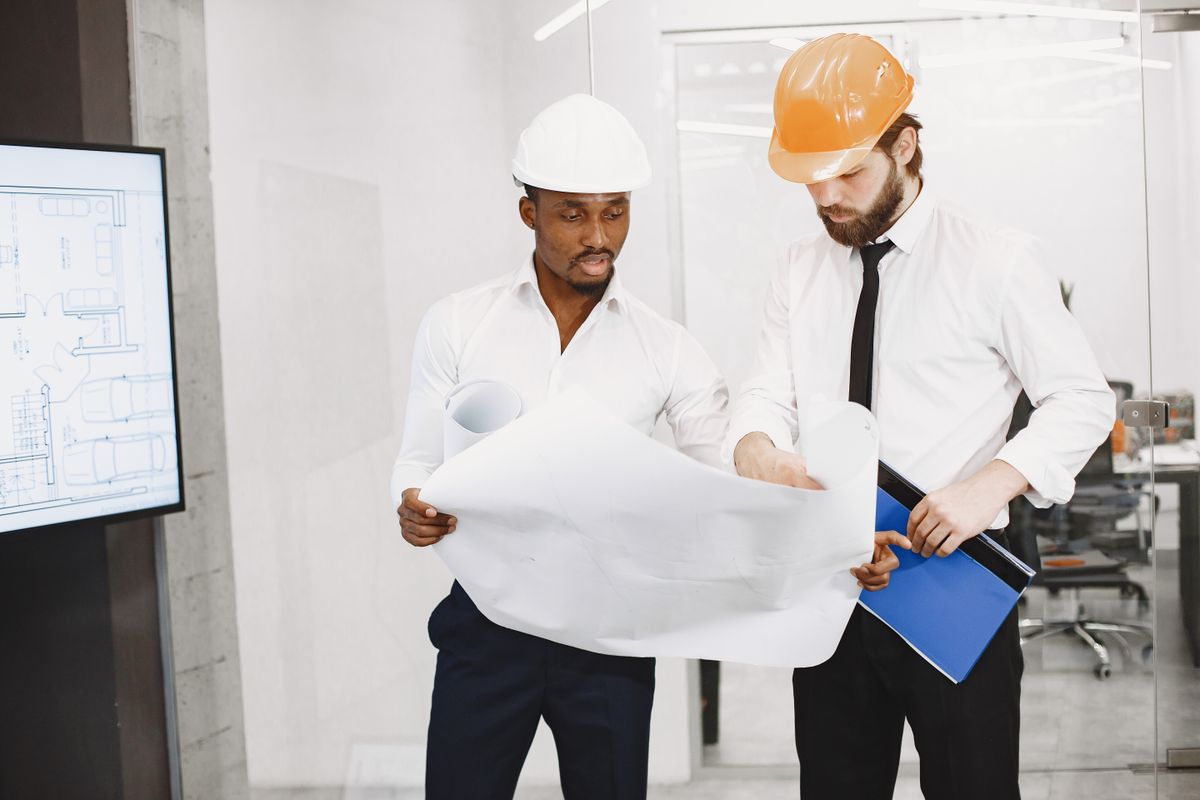 Two architects in hard hats discussing a blueprint together in an office