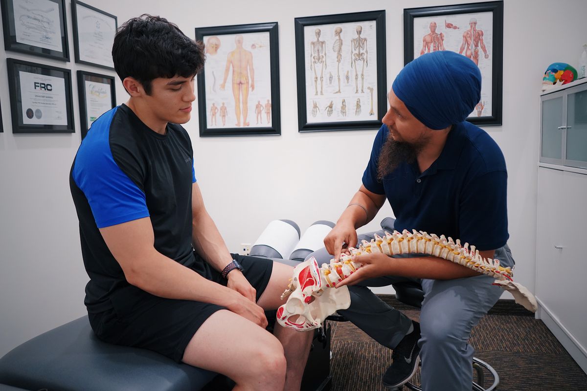 Chiropractor using a spine model to explain a treatment plan to a patient in an Edinburgh clinic