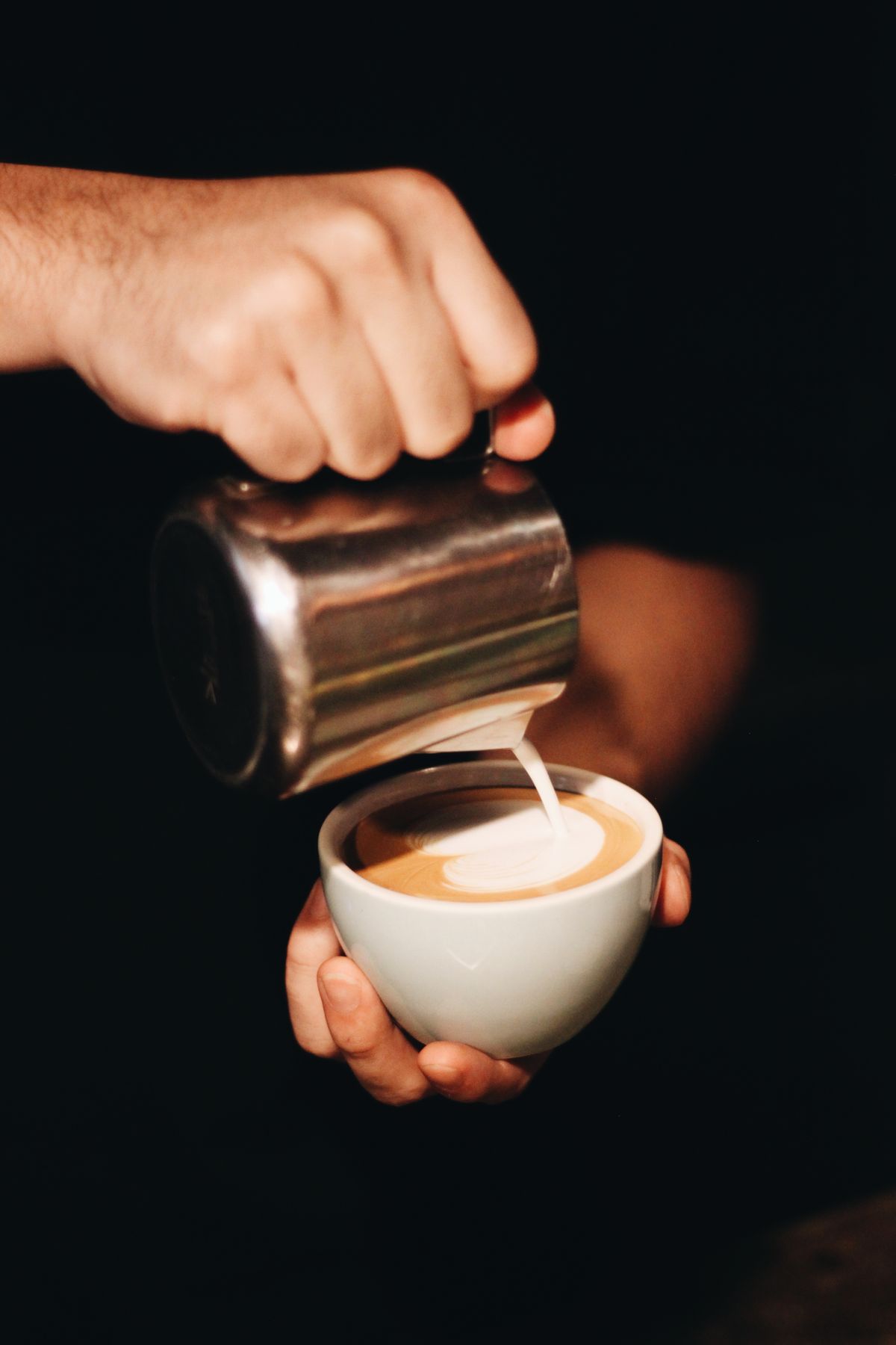 Barista pouring latte art into a coffee cup behind the counter
