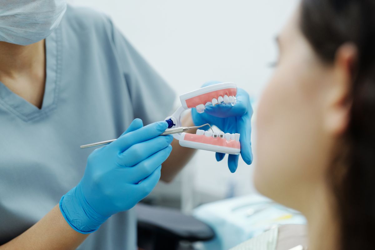 Dentist in blue gloves showing a teeth model to a patient during consultation