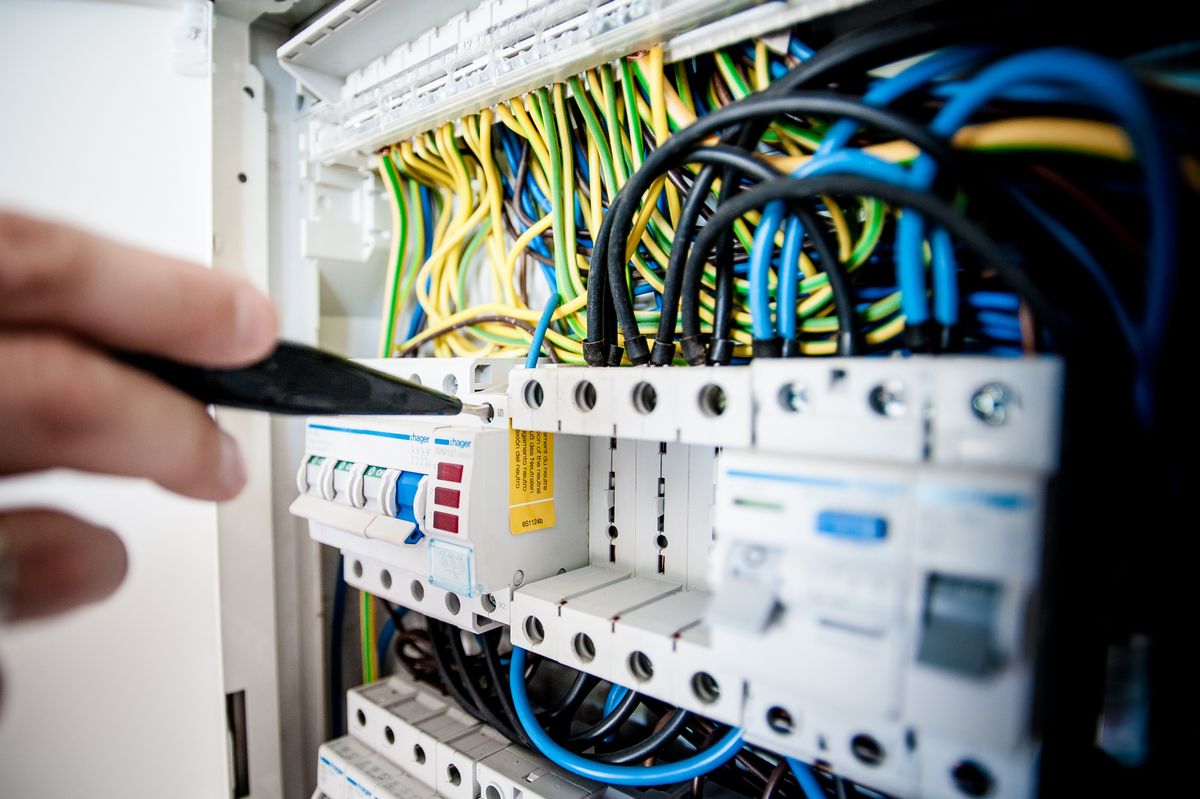 Electrician fixing an opened switchboard with colour-coded wiring