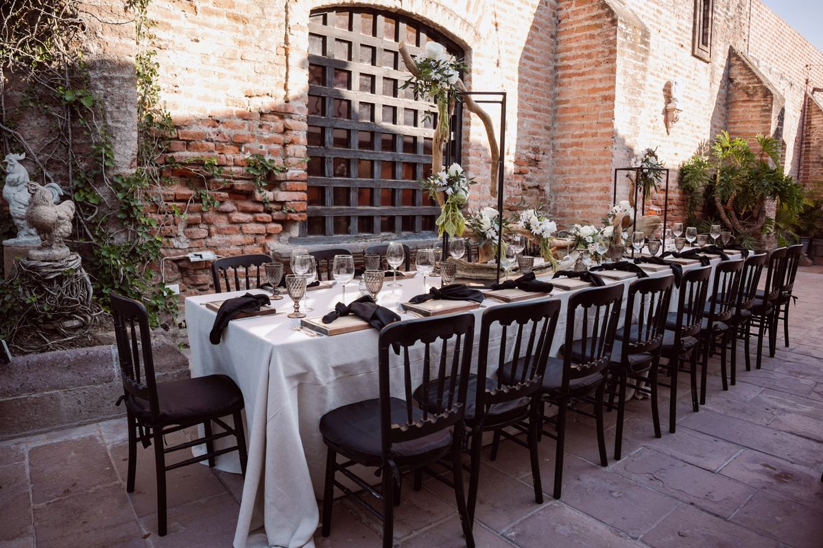 Elegant outdoor wedding reception table setup styled by an event planner, with floral centrepieces and black chairs