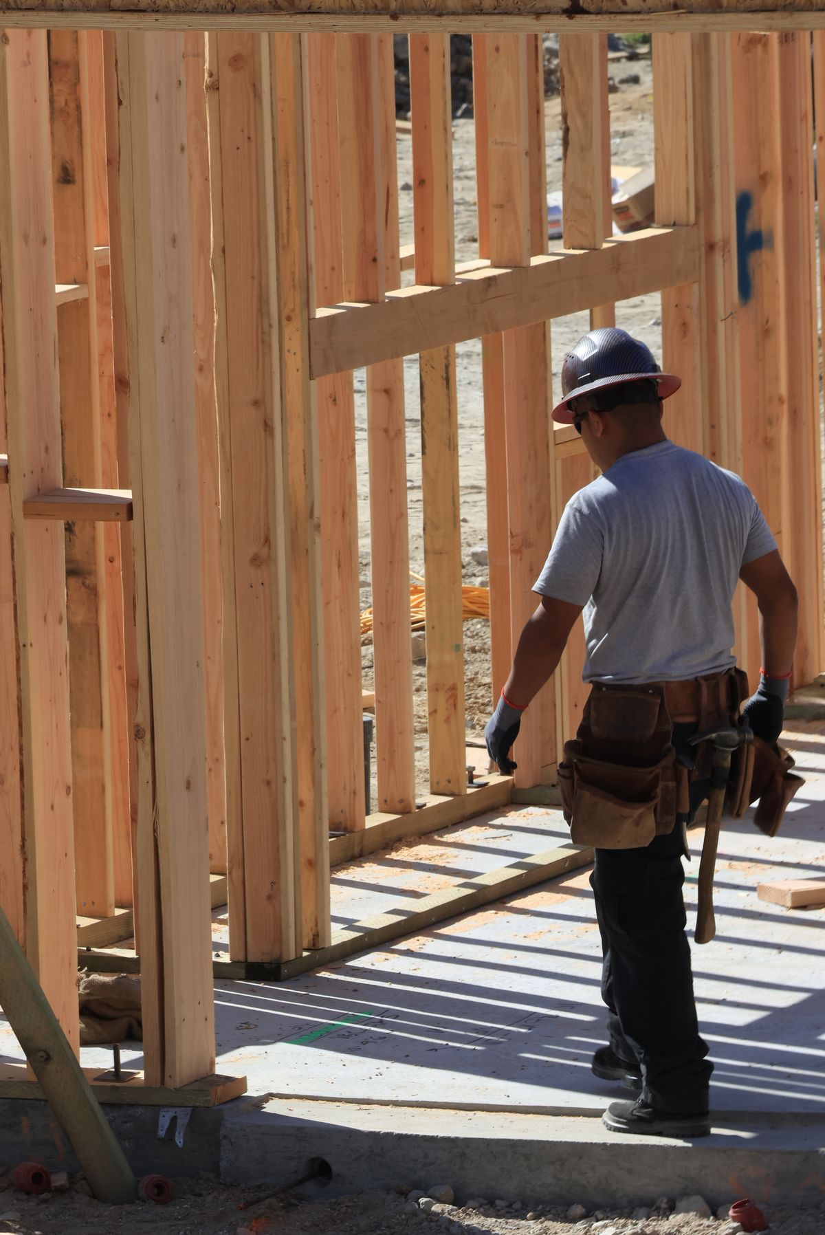 Builder in safety helmet and tool belt framing a new house on site