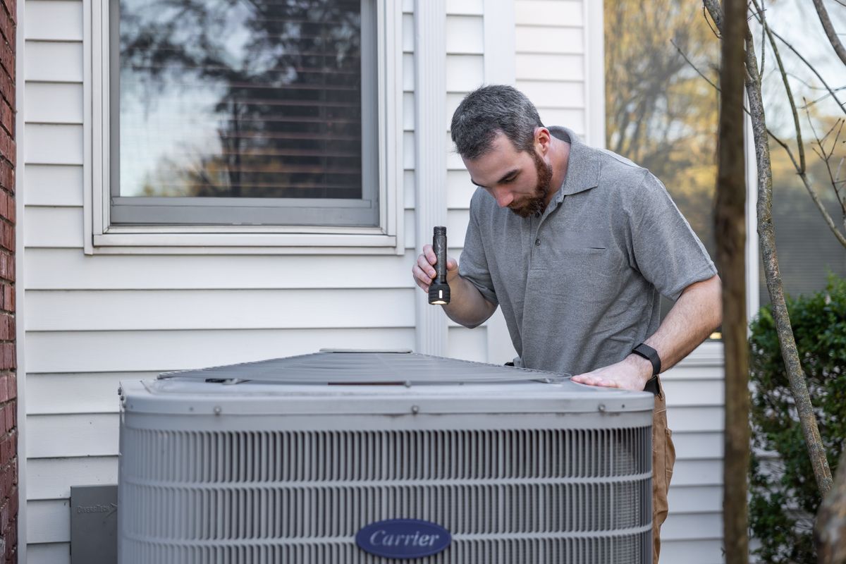 HVAC technician inspecting an outdoor condenser unit during a service visit