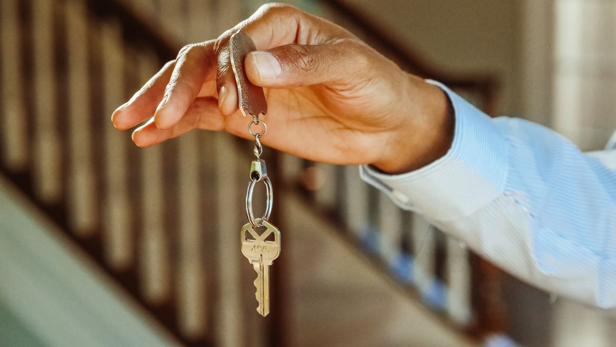 Person holding a single silver door key on a keychain after a lock change