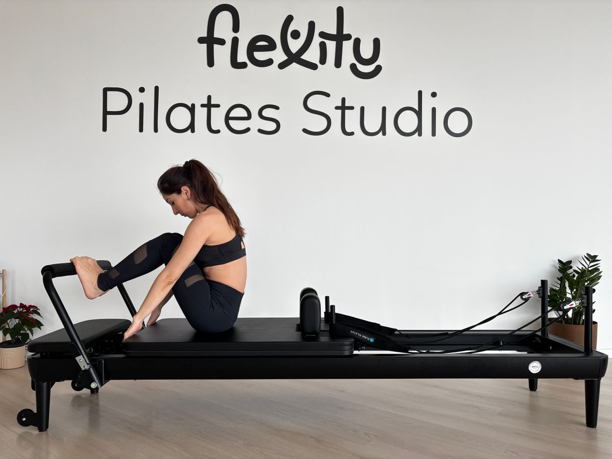 Woman practising Pilates on a reformer machine in a bright studio
