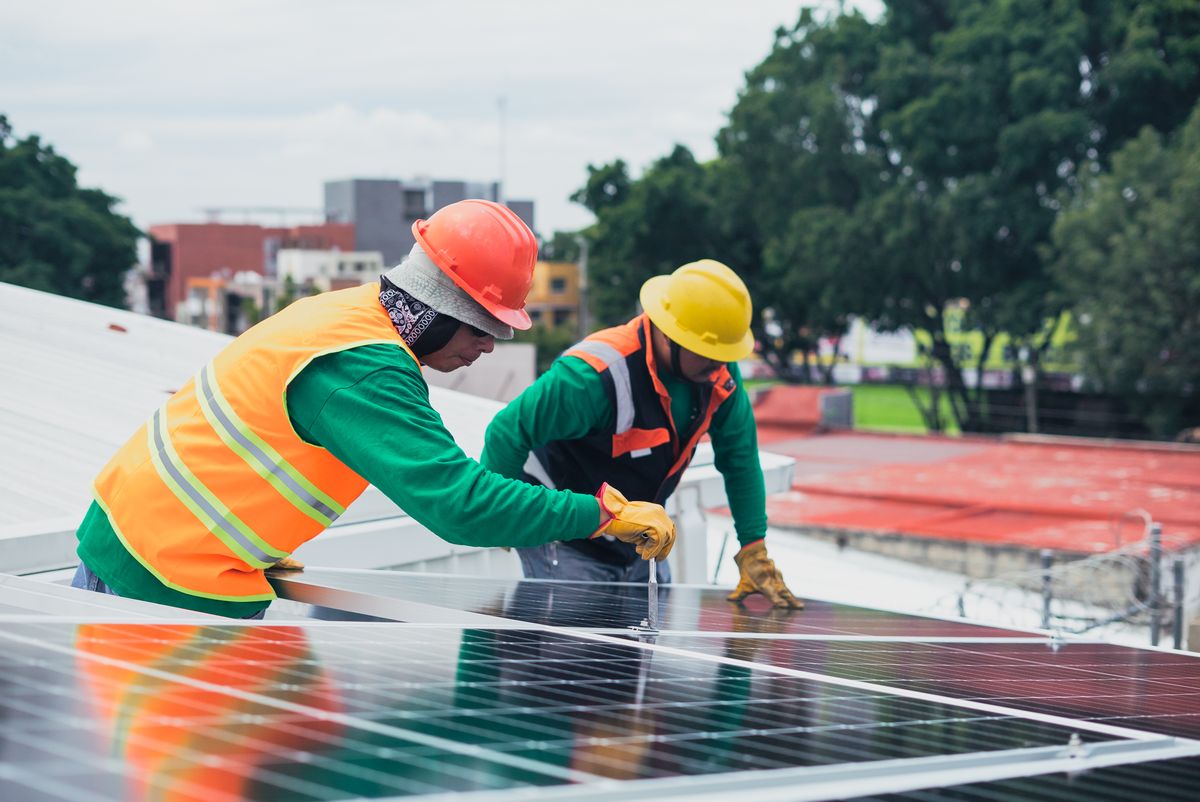 Two solar installers fitting rooftop solar panels wearing safety harnesses