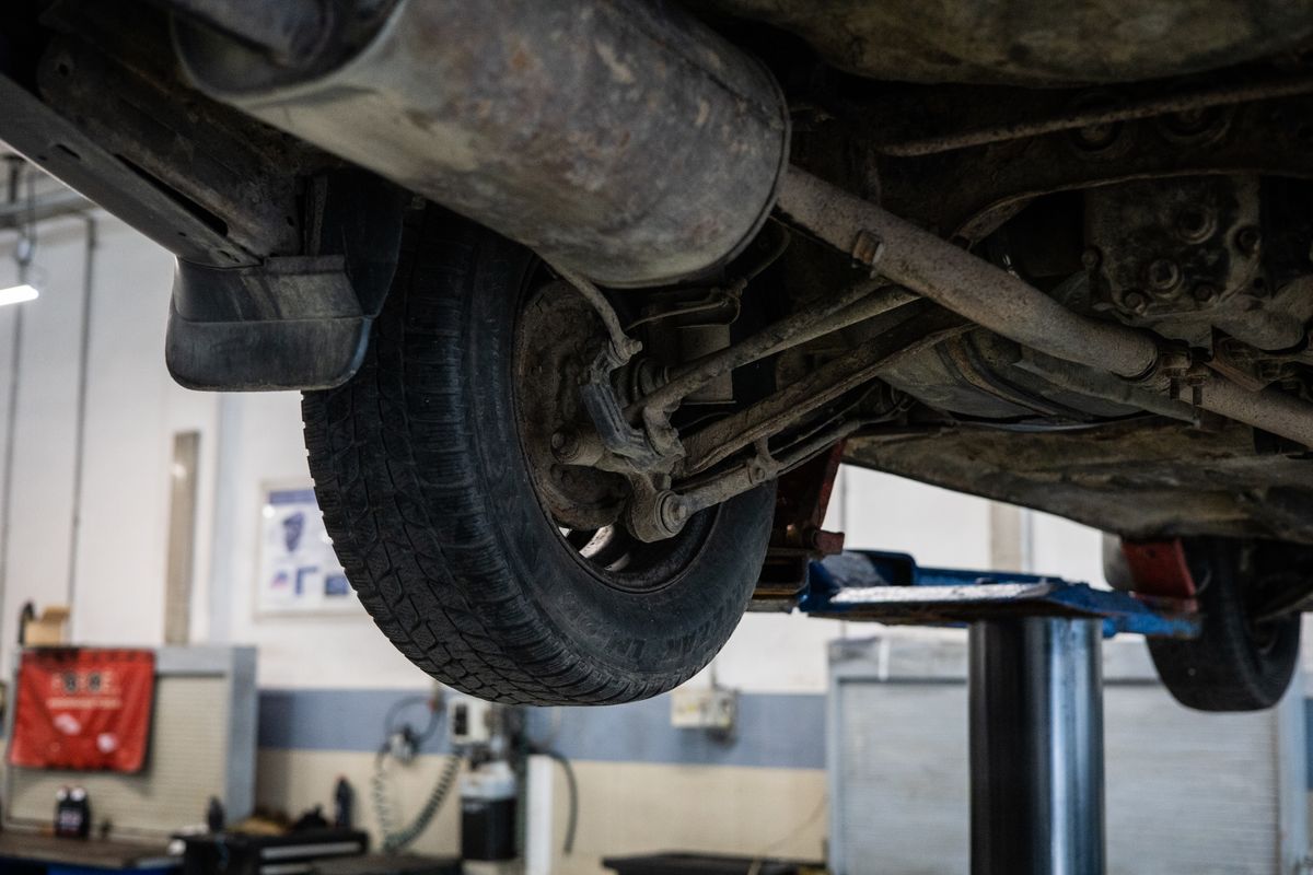 Technician working underneath a vehicle on a workshop ramp during tyre service