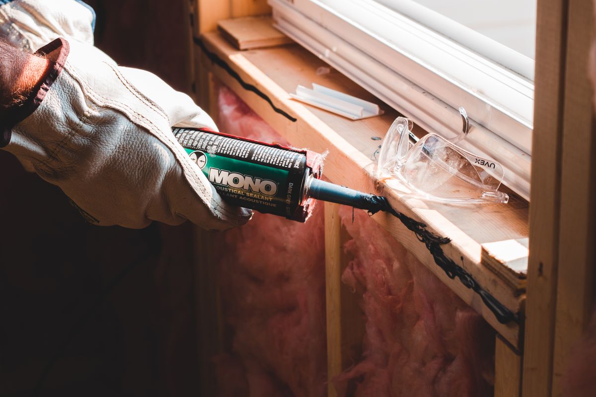 Tradesperson applying weatherproof sealant around the frame of a replacement window