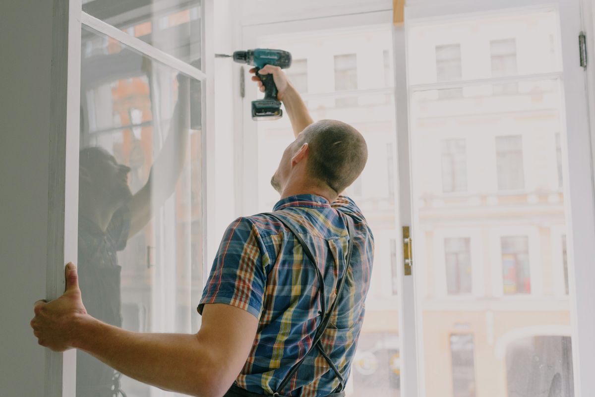 Handyman using a drill to fix a new window frame into place inside a house